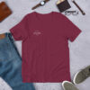 A mahroon tshirt with the logo rapstitches and objects like jeans, glasses, shoes and wallet in the background
